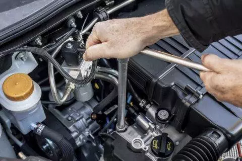 Two hands operating a wrench to remove or tighten a bolt in a latest generation automobile engine